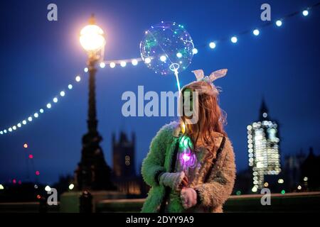 Eine Frau hält einen beleuchteten Ballon auf der South Bank in London. Millionen weitere Menschen zogen zu härteren Coronavirus-Beschränkungen um, als die neuen Tier-Änderungen in England in Kraft traten. Stockfoto