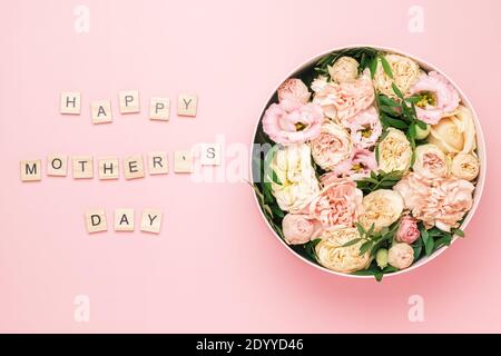 Happy Mothers Day Schriftzug auf den hölzernen Quadraten mit Buchstaben auf dem rosa Hintergrund und große runde Box mit roten Blumen und Rosen. Grußkarte Stockfoto