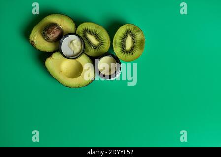 Kiwi-Samen, Avocado-Birne und Traubenöl Augencreme zur Behandlung der Augenpartien. Augencreme und in Scheiben geschnittene Kiwi und Avocado auf grünem Hintergrund im Studio Stockfoto
