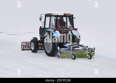 Radtraktor mit Schneepflug und mechanischer Kehrmaschine Bewegt sich auf einem verschneiten Hintergrund Stockfoto