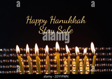 Brennende Kerzen auf einem dunklen Hintergrund und Text Happy Hanukkah Stockfoto