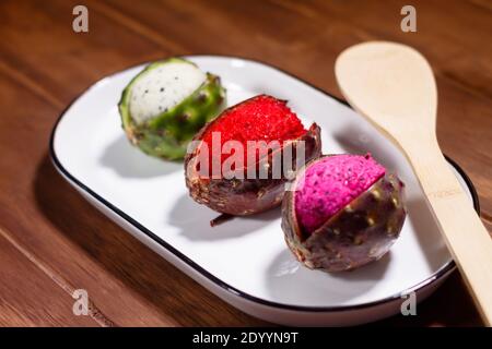 Mexikanische exotische Früchte. Die Pitaya wächst auf einem Kaktus. Die Pitayas sind in weißer Platte über einem Holztisch ausgestellt Stockfoto