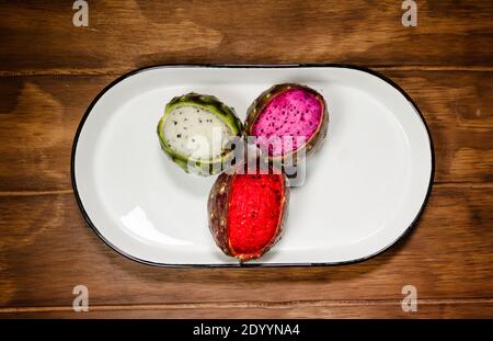 Mexikanische exotische Früchte. Die Pitaya wächst auf einem Kaktus. Die Pitayas sind in weißer Platte über einem Holztisch ausgestellt Stockfoto