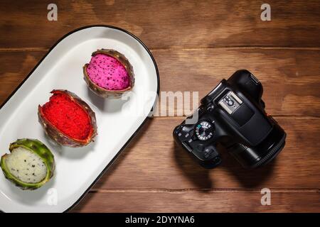 Mexikanische exotische Früchte. Die Pitaya wächst auf einem Kaktus. Die Pitayas sind in weißer Platte über einem Holztisch neben einer Fotokamera ausgestellt Stockfoto