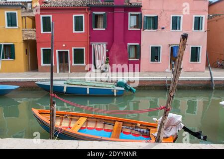 Zwei kleine Motorboote dockten an der Seite eines Kanals an, der von bunt bemalten Häusern auf der Insel Burano umgeben ist, die in der Nähe von Venedig, Italien, liegt. Stockfoto