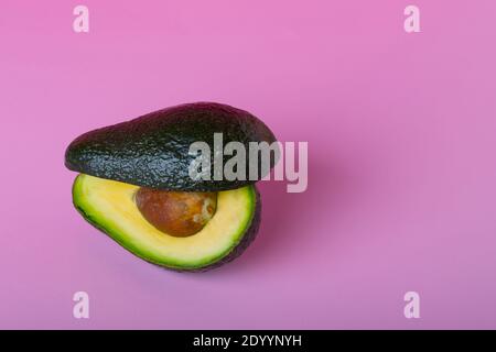 Avocado Frucht zweigeteilt auf rosa Hintergrund. Grüne Avocado, minimalistischer flacher Lay-Style. Stockfoto