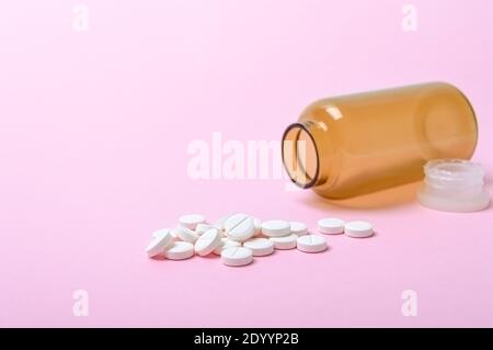 Weiße runde Pillen aus einer braunen Flasche auf einem rosa Hintergrund verstreut. Thema Pharmazie und Gesundheitswesen. Medizinischer Hintergrund. Speicherplatz kopieren. Stockfoto