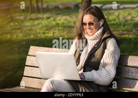 Glückliche Frau, die im Stadtpark mit einem Laptop arbeitet. Freiberufliches Arbeitskonzept Stockfoto