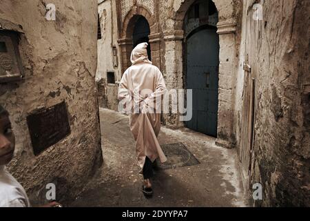 MAROKKO / Essaouira / traditionell gekleideter Mann bei einem Spaziergang in einer typischen schmalen Streette der Medina (Altstadt) in Essaouira. Stockfoto