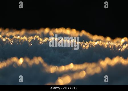 Abstrakter Hintergrund von Schneekristallen in goldenem Sonnenlicht bei Sonnenaufgang an einem frostigen Wintermorgen. Ein Muster aus blauen goldenen Kristallen von Frost Nahaufnahme. Stockfoto