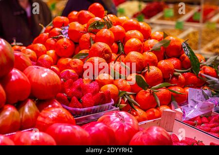 Erdbeeren und Mandarinen in der Hauptaufnahme mit Tomaten in Der Hintergrund an einem Marktstand nicht im Fokus Stockfoto