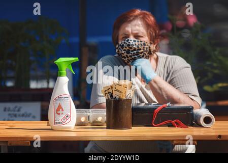 Desinfektionsmittel auf dem Tisch vor der alten Verkäuferin mit Stoffmaske auf dem Straßenmarkt. Stockfoto