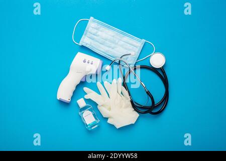 Digitales berührungsloses Thermometer, Schutzmaske, Latexhandschuhe, medizinisches Stethoskop und Desinfektionsmittel auf blauem Hintergrund. Banner. Draufsicht, flach liegend. Stockfoto