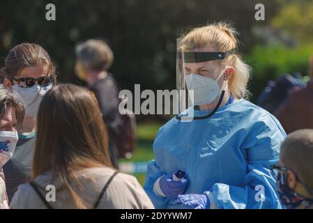 Junge Sanitäterin mit Digitalthermometer in der Hand, die mit einer Frau spricht, die in der Schlange für den Corona-Virus-Test wartet. Stockfoto