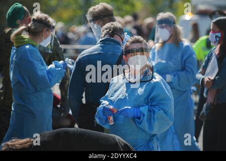 Sanitäter, Soldaten und eine Reihe von Menschen mit Stoffmasken an einem Ort, an dem Corona-Virus-Tests stattfinden. Stockfoto