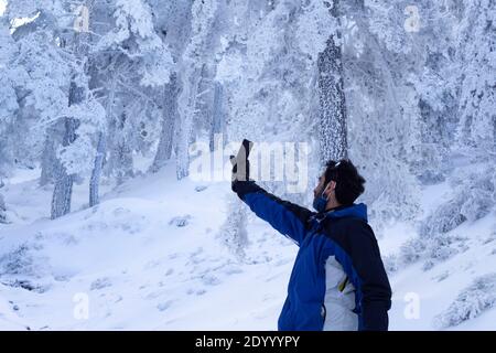 Ein Mann mittleren Alters sucht auf einem verschneiten Berg nach WLAN-Signal. Der Mann trägt eine Maske gesenkt. wifi-Verbindung in der tiefen Natur Stockfoto