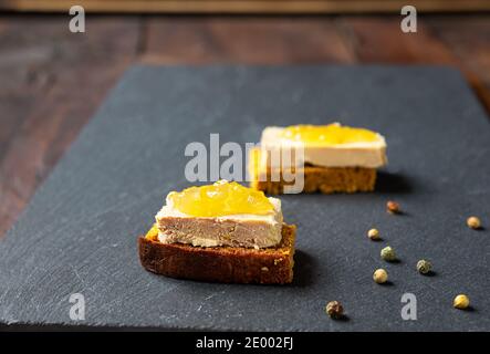 Foie Gras Toasts mit kandierten Zwiebeln und Pfefferkörnern auf einem Schiefer Stockfoto