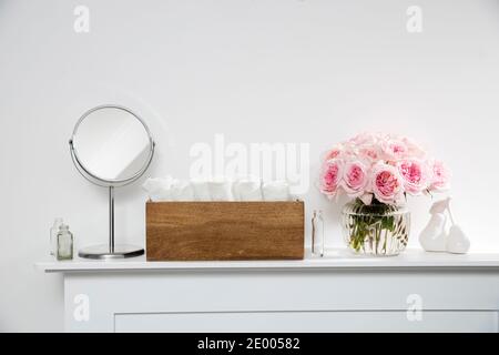 Rosa Weiß Rosa O'hara in der runden Glas transparente Vase ist auf dem Kamin. Weiße Frottee-Handtücher in einer Holzkiste im Spa-WC. Die Flasche Stockfoto