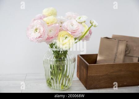 Das Bouquet von rosa und gelben persischen Butterblumen isoliert auf hellgrau in der Glas runde Vase mit Holzkiste mit eingewickelten Geschenken. Speicherplatz kopieren Stockfoto