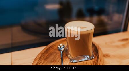 Kaffee Latte mit Schaum und Milch in einem transparenten Glas Steht auf einem Holztablett mit einem Löffel auf dem Tabelle Stockfoto