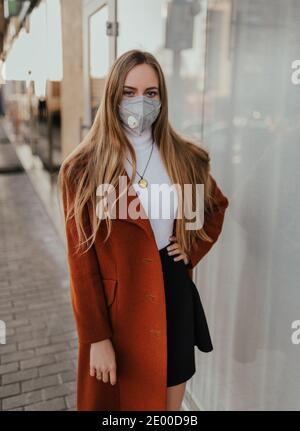 Junge ukrainische blonde Frau in schützende medizinische Maske kn95 Atemschutzmaske auf der Straße vor dem Hintergrund der Schaufenster. Coronavirus-Infektion. Zubehör Stockfoto