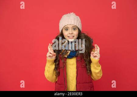 Überrascht hübsches Mädchen in Kugelweste mit Strickmütze und Pullover Daumen drücken, einen Wunsch machen. Stockfoto