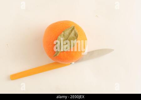 Draufsicht, eine ganze Mandarine mit grünem Blatt und einem Messer zum Schneiden. Stockfoto