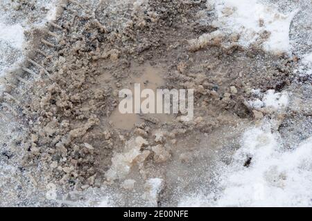 Nahaufnahme einer Schuttstraße mit Schlaglöchern, großen schlammigen Pfützen und geschmolzenem Schnee. Hochwertige Fotos Stockfoto