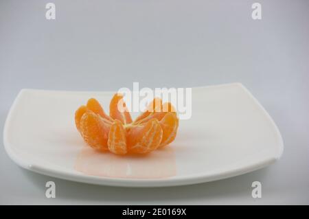 Eine weiße Platte mit Scheiben einer geschälten Mandarine auf Ein neutraler Hintergrund und ein Kopierbereich Stockfoto