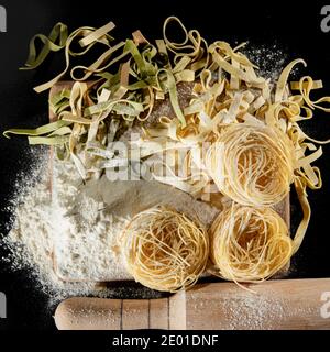 Frisch gekochte Pasta liegt auf einer dunklen, mit Mehl bestäubten Oberfläche. Italienische Pasta. Tagliatelle. Rohe Pasta. Italienische Pasta Rezept. Draufsicht, Kopierbereich Stockfoto