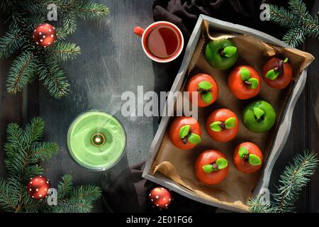 Marzipan Schwamm Äpfel. Weihnachtsdessert mit Tasse Tee, Tannenzweigen, grüner Kerze, Tannenzapfen, weichem Stern. Draufsicht auf rustikales Holztablett auf Textil Stockfoto