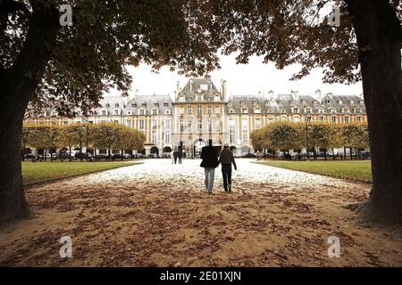 FRANCE / IIe-de-France/Paris/ Le Marais/ Paar, das Hand in Hand auf dem Place des Vosges schlendert, gesäumt von eleganten Stadthäusern. Stockfoto