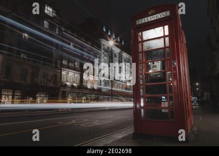 Eine klassische Londoner Telefonbox bei Nacht, während Doppeldeckerbus fährt, indem er leichte Wege hinter sich lässt. Stockfoto