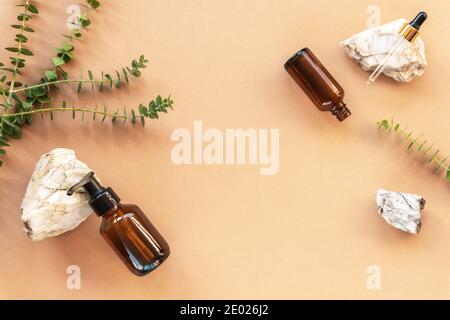 Natürliche Bio-Kosmetik. Flaschen aus schwarzem Glas ohne Markennamen mit Natursteinen und Eukalyptusblättern. Home Spa-Konzept Stockfoto