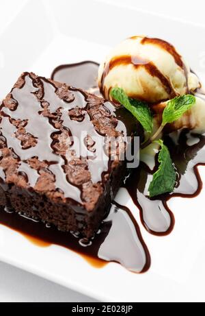 Vegane Schokolade-Brownie-Dessert mit milchfreiem Kokosmilch-Vanilleeis Creme mit Karamellsauce auf weißem Hintergrund im Studio Stockfoto