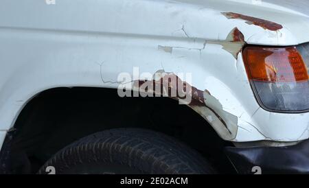 Beschädigt durch Kratzer, abblätternde Farbe und Rost am vorderen Kotflügel eines Autos Stockfoto