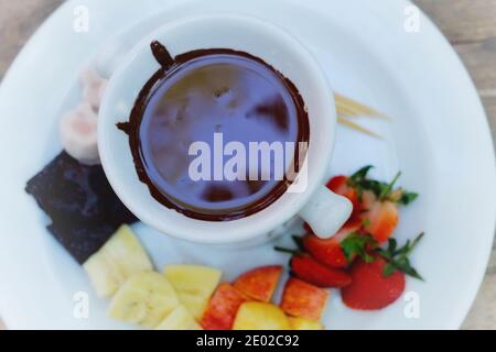 Die Draufsicht auf eine Reihe von Schokolade Fondue mit Früchten und Kuchen und Zahnstocher zum Eintauchen in heiße Schokolade mit weißem Teller und Topf. Stockfoto