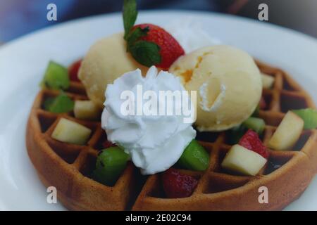 Ein Teller mit gesundem Dessert mit einer runden Waffel, serviert mit Eiscreme, Peitschencreme und verschiedenen gehackten Früchten. Stockfoto