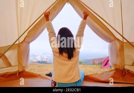 Eine junge Frau sitzt friedlich in ihrem weißen Zelt am Morgen mit kühler Brise und Morgensonne, Stretching und entspannend. Stockfoto