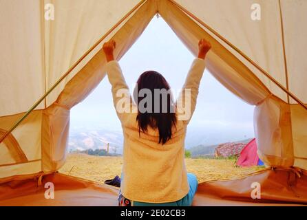 Eine junge Frau sitzt friedlich in ihrem weißen Zelt am Morgen mit kühler Brise und Morgensonne, Stretching und entspannend. Stockfoto