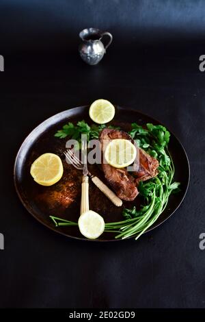 Gebratener Karpfen mit Zitrone und grüner Petersilie auf schwarzem Hintergrund. Traditionelles polnisches Gericht für Heiligabend. Stockfoto