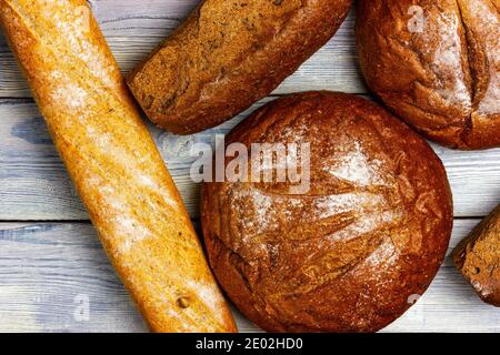 Eine Auswahl an frischen knusprigen Broten. Blick von oben. Brottheke bei der Bäckerei. Roggenbrot, Baguette auf einem hellen Holztisch. Stockfoto