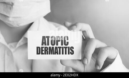 Atopische Dermatitis auf einer Karte, die von der Hand des Arztes gehalten wird. Arzt trägt chirurgische Medizin Gesichtsmaske. Medizinisches Konzept. Stockfoto