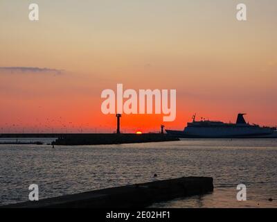 Das Schiff betritt die Meeresbucht vor der Kulisse von Die untergehende Sonne und Vögel kreisen über dem Meer Stockfoto