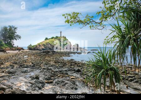 Schöne Aussicht auf den alten weißen Leuchtturm an der felsigen Küste. Blick durch die Vegetation. Landschaft von Lanta Island in Thailand. Stockfoto