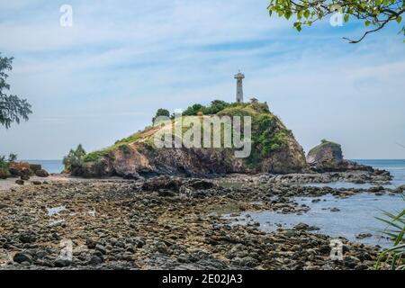 Ein alter Leuchtturm auf einer Klippe in der Nähe eines felsigen Ufers. Der Felsen ist mit viel Grün bedeckt. Wunderschöne Meereslandschaft von Koh Lanta Insel in Thailand. Stockfoto