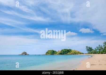 Ein wunderschöner und menschenverlasser tropischer gelber Sandstrand. Türkisfarbenes Meer und blauer Himmel mit Wolken. Ein weißer Leuchtturm auf einer Klippe in der Ferne. Koh Lanta, Stockfoto