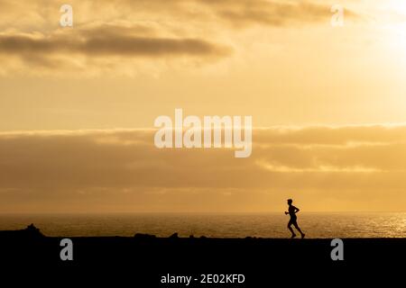 Silhouette eines unerkennbaren Mannes, der bei Sonnenuntergang auf Lanzarote, Kanarische Inseln, Spanien vor dem Meer läuft. Gesundheit und Sport im Freien concep. Stockfoto