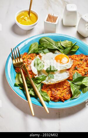 Kürbispfannkuchen mit gebratenen Eiern und Grüns, serviert auf einem blauen Teller auf einem Marmortisch, amerikanisches Frühstück am Morgen, vertikaler Blick von oben Stockfoto