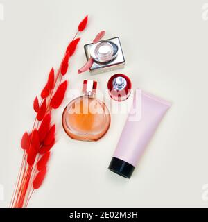 Verschiedene Parfüm-Flaschen, rosa Squeeze-Flasche Kosmetikschlauch mit schwarzer Kappe und roten Kräutern Lagurus auf Elfenbeintisch. Beauty Flatlay, Draufsicht, Mockup. Stockfoto